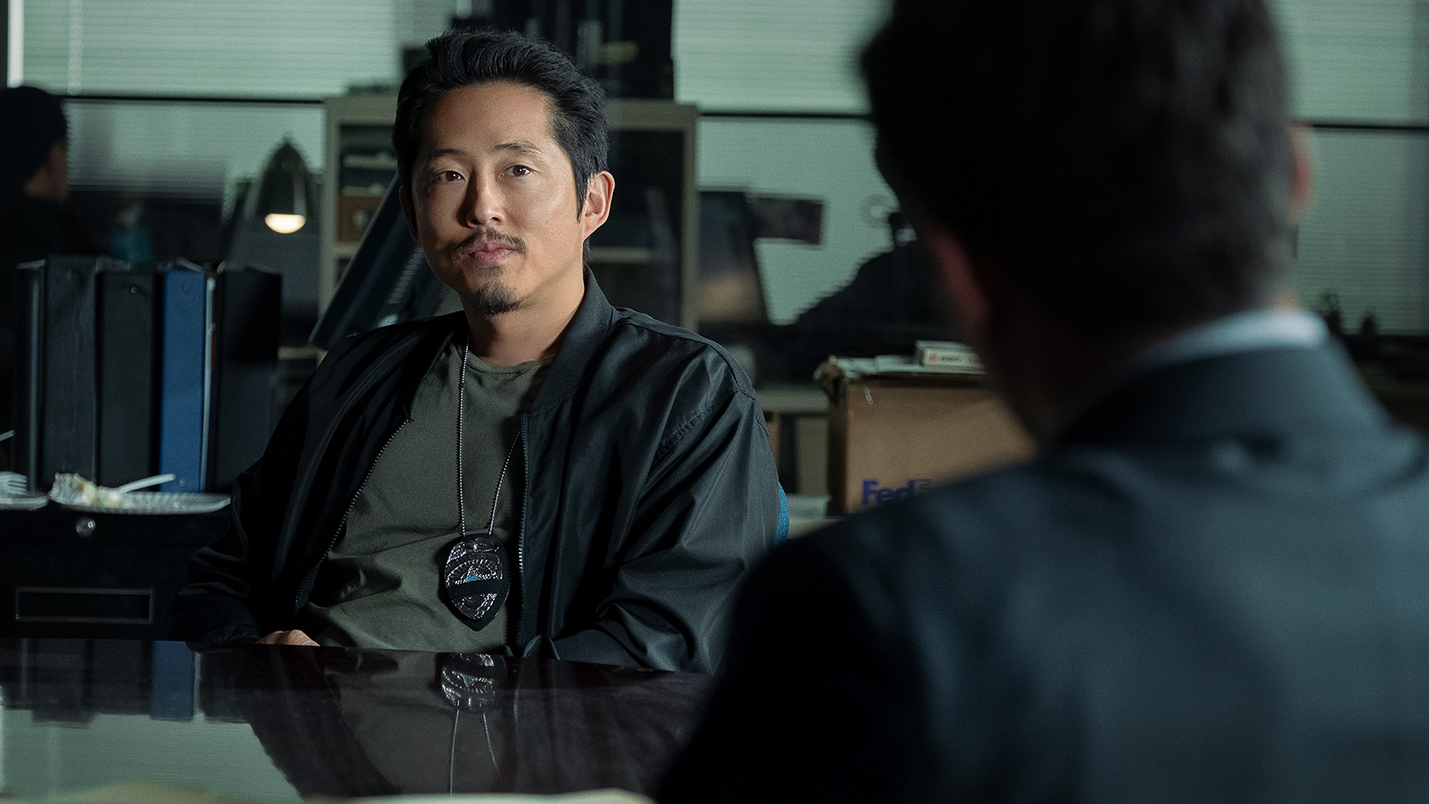 Steven Yeun's Mike Ro sitting opposite Scott Adkins' Del Byrne in Netflix's The RIP