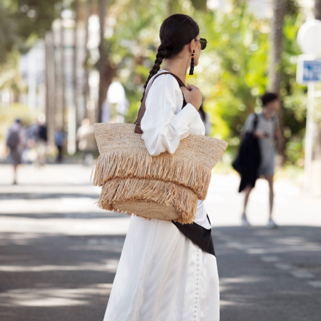 CANNES, FRANCE - MAY 21: Gili Biegun wears long white and cream silk maxi dress with multiple small buttons, black-and-white silk scarf tied around the waist, oversized raffia beach bag with fringe and brown leather straps, black tassel bead earrings, black flip-flop kitten heels from AGL, and black Ray-Ban sunglasses during the 79th annual Cannes Film Festival on May 21, 2026 in Cannes, France. (Photo by Raimonda Kulikauskiene/Getty Images)