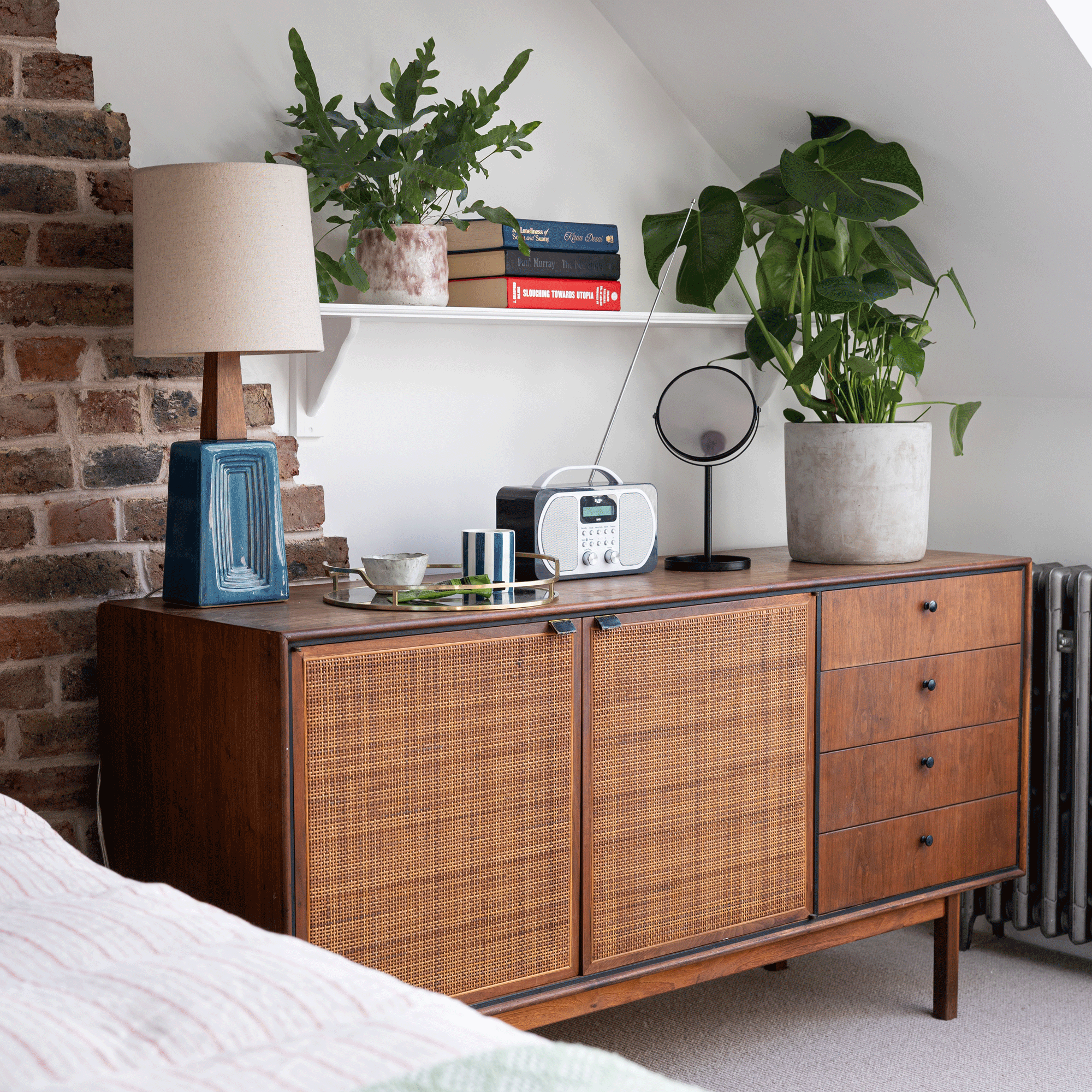 a loft room with a retro sideboard topped with a radio, lamp, plant and mirror