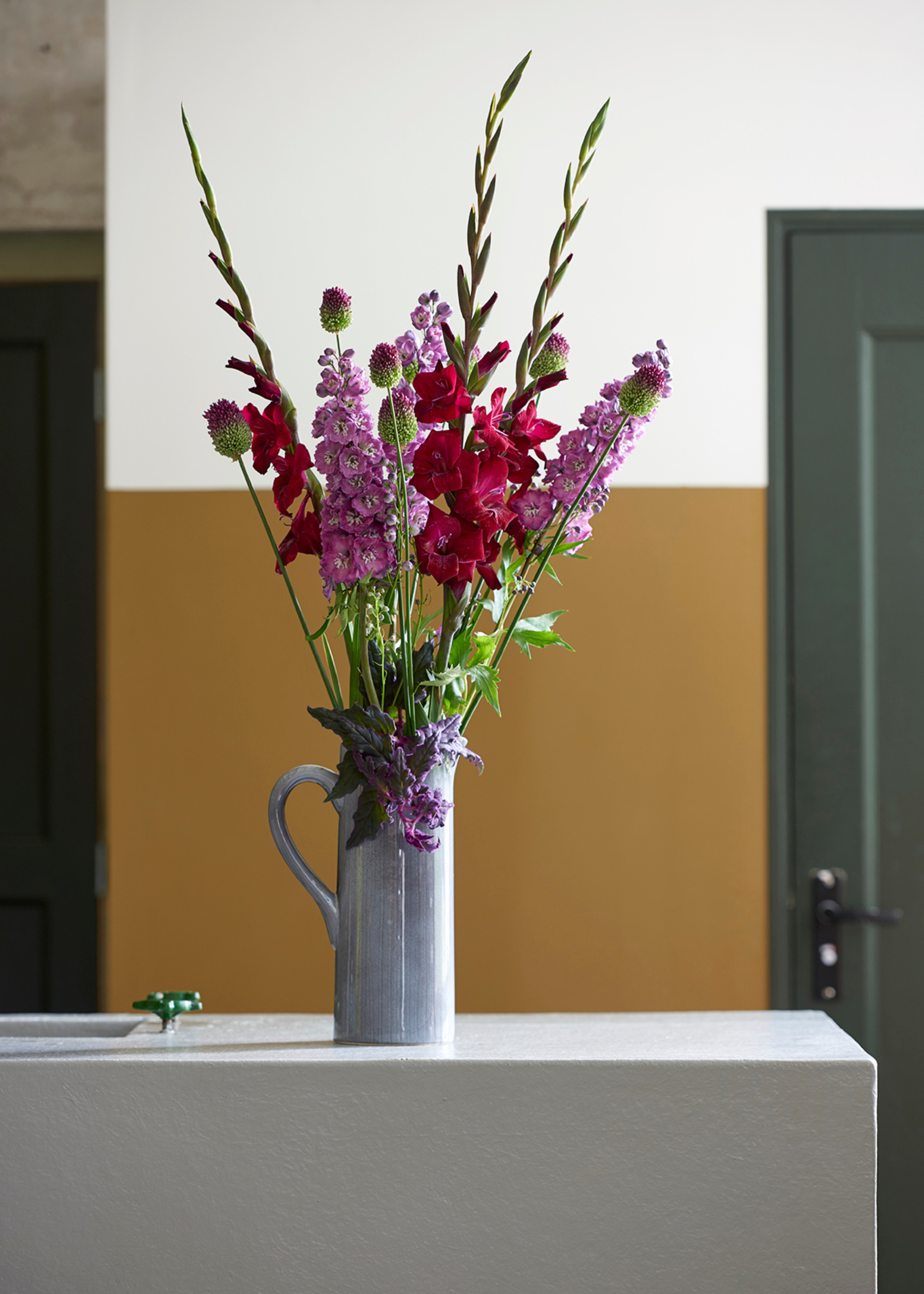 A tall vase with a handle filled with larkspur and colorful flowers on a kitchen island