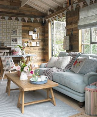 Garden shed ideas with indoor sitting room furnishings, including a pale blue sofa, wooden coffee table and floral fabric accents.