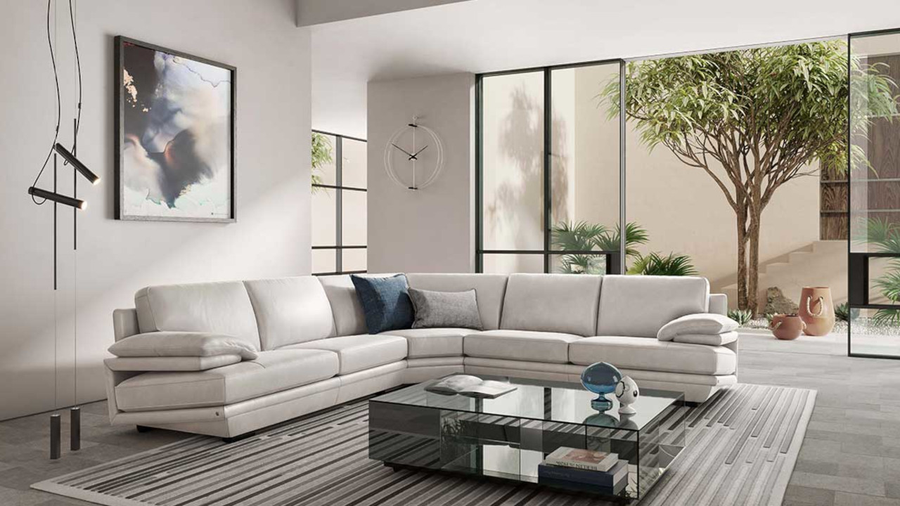 natuzzi plaza sofa in a living room with steel frame doors leading to a courtyard with a tree, gray timber floorboards, gray striped rug under glass coffee table, and white walls with artwork