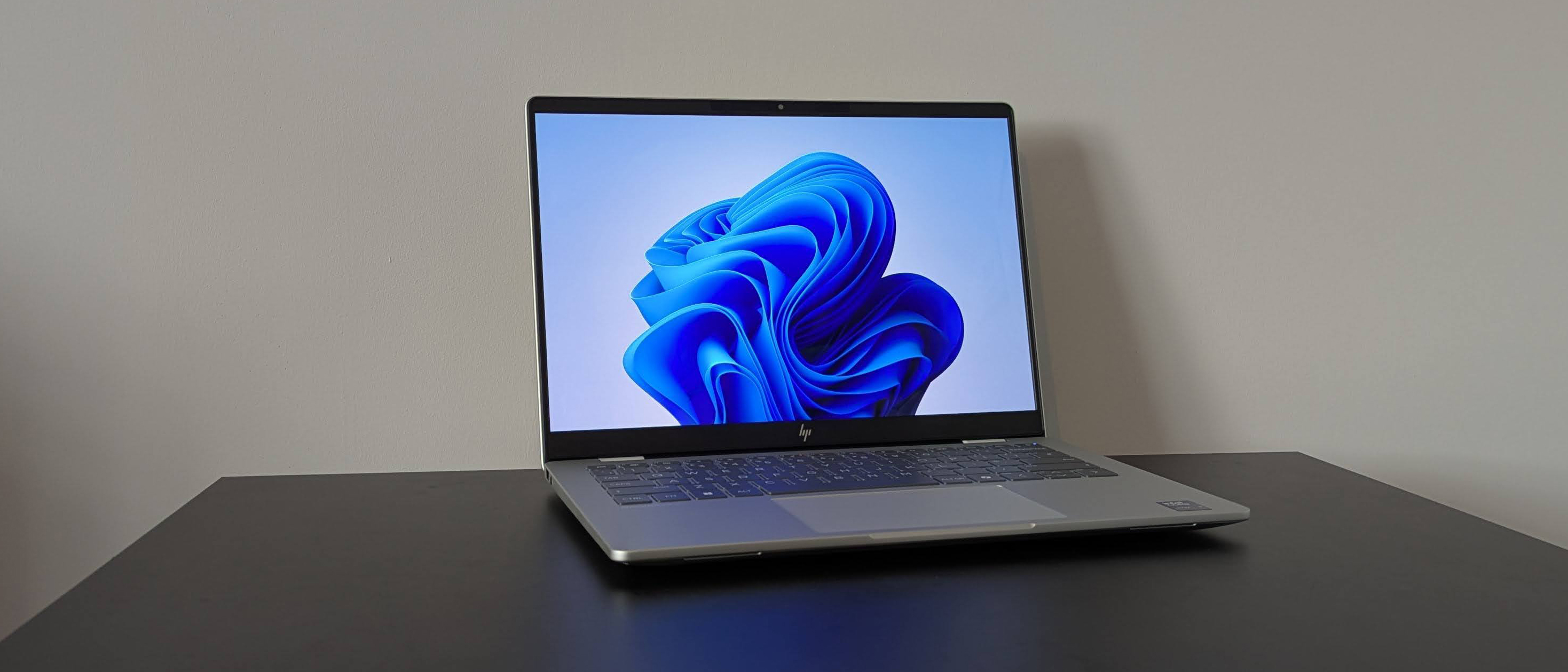 Three-quarter view of HP OmniBook 7 14-inch open on black desk with white wall in background