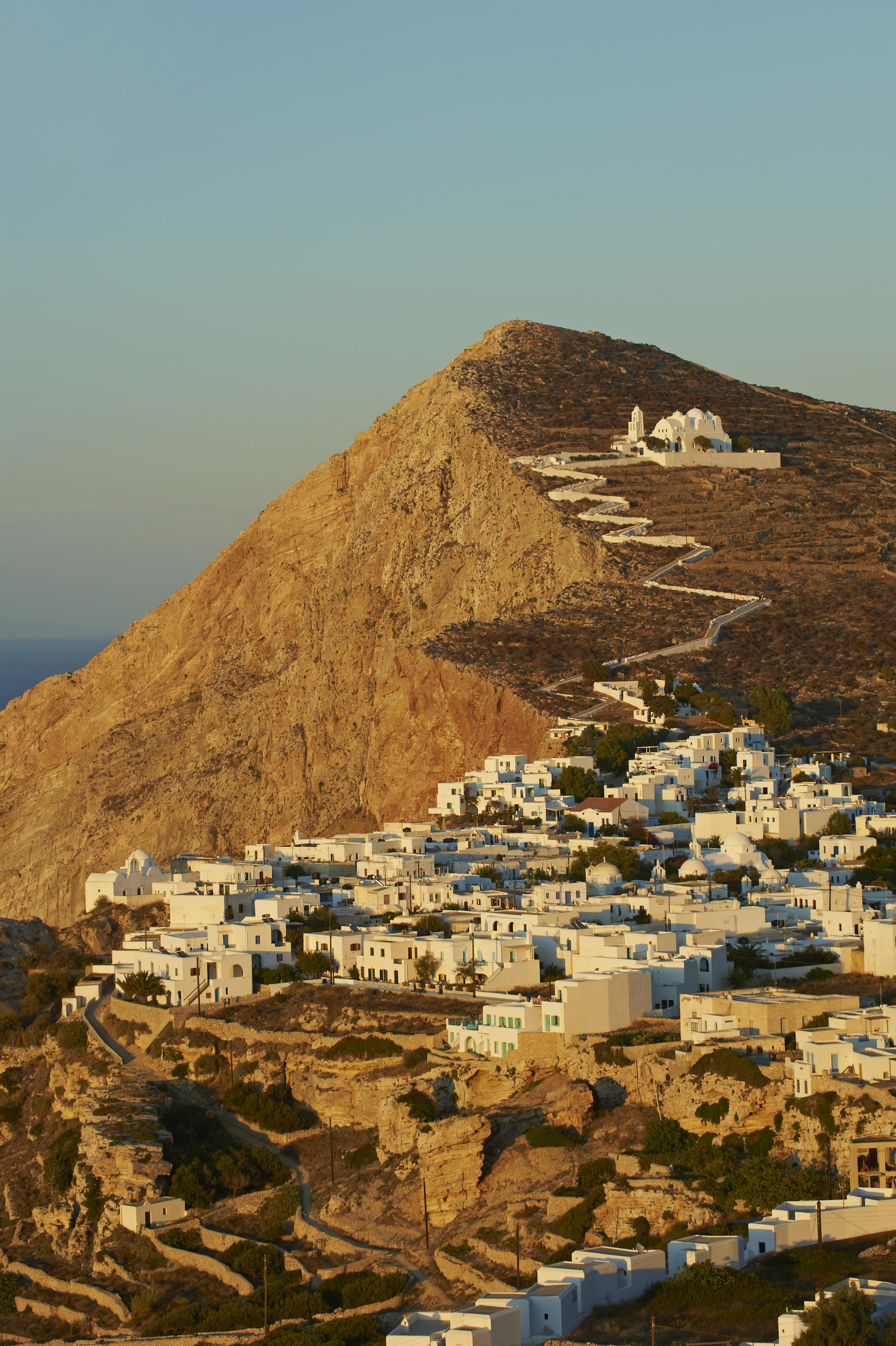 A Greek hilltop town made up of white houses and a winding marble path and small cathedral