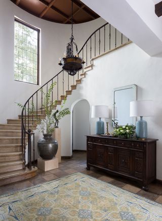 traditional curved stone staircase with iron handrail and antique style pendant light panelled wood ceiling and dark wood console and oriental style rug
