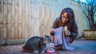 a woman feeds her cat outside