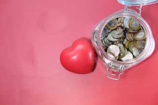 A jar filled with coins, which will be donated to charity, beside a love heart