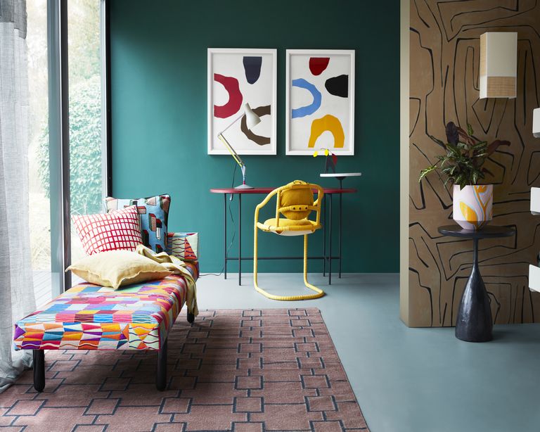 teal painted room with desk area and chaise longue, geometric patterns on walls and on pink rug