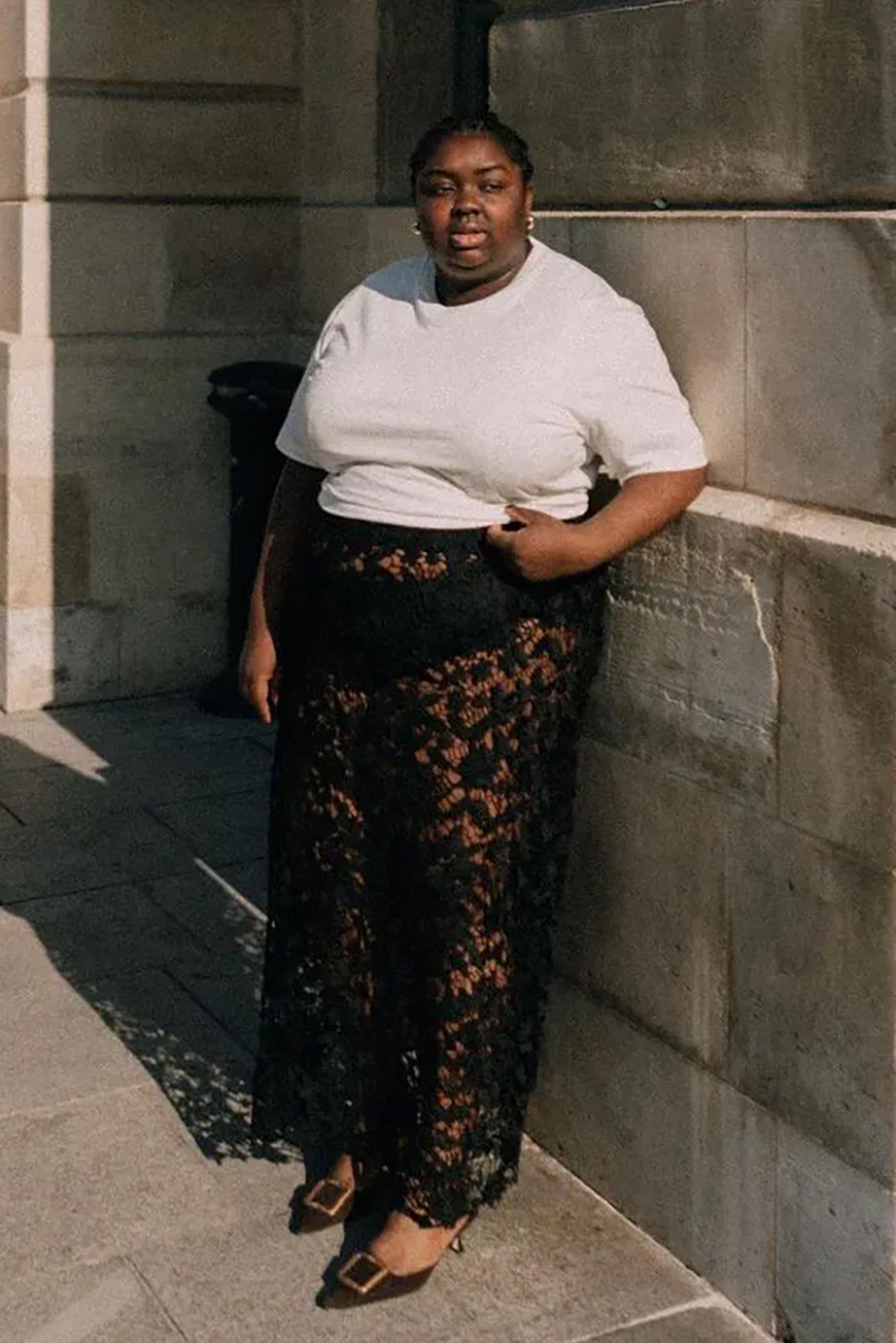 a woman wearing a white t-shirt, sheer lace skirt, and brown buckle kitten heel mules