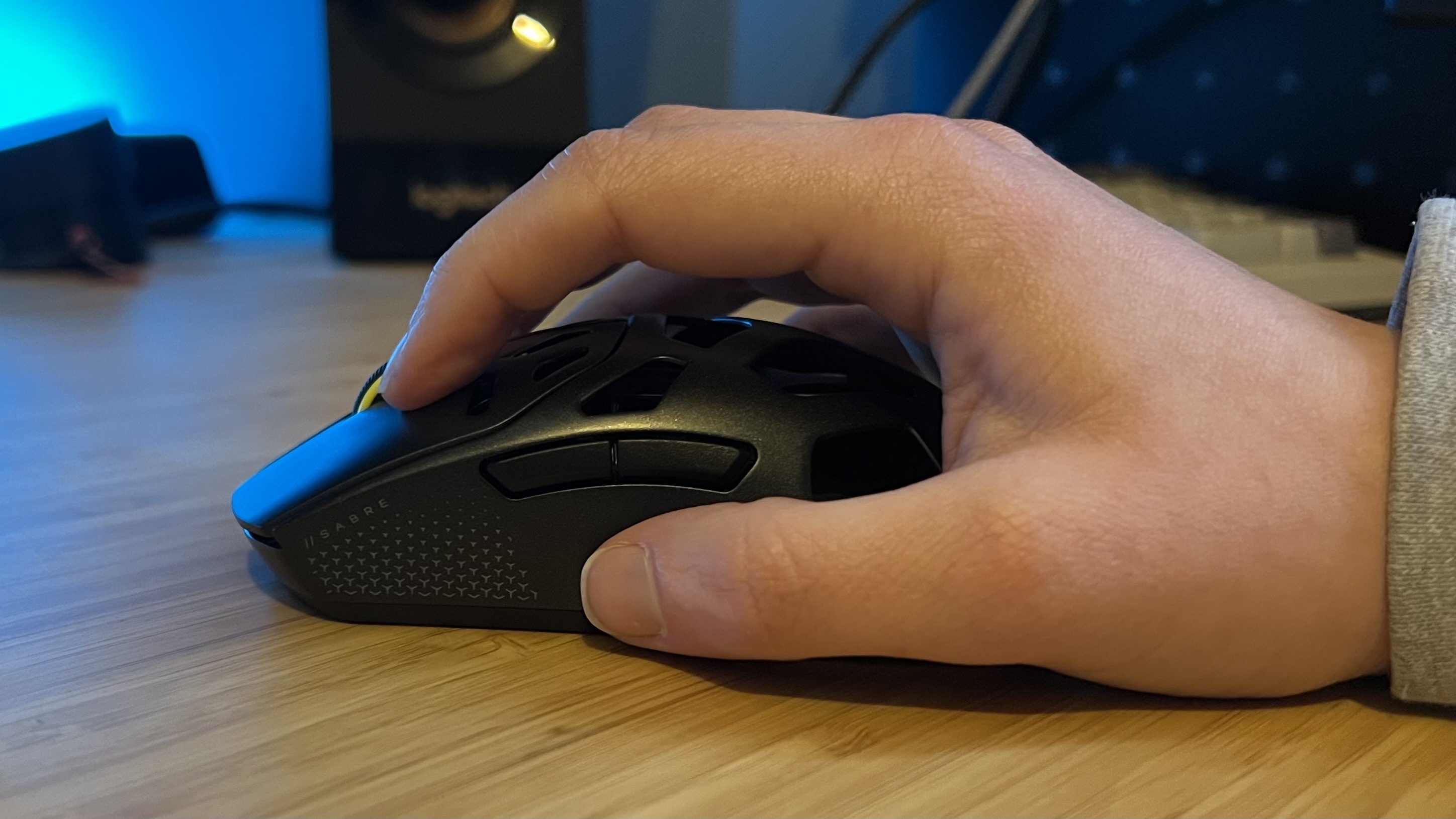 Hand using Corsair Sabre V2 Pro Wireless MG gaming mouse in a claw grip on a wooden desk