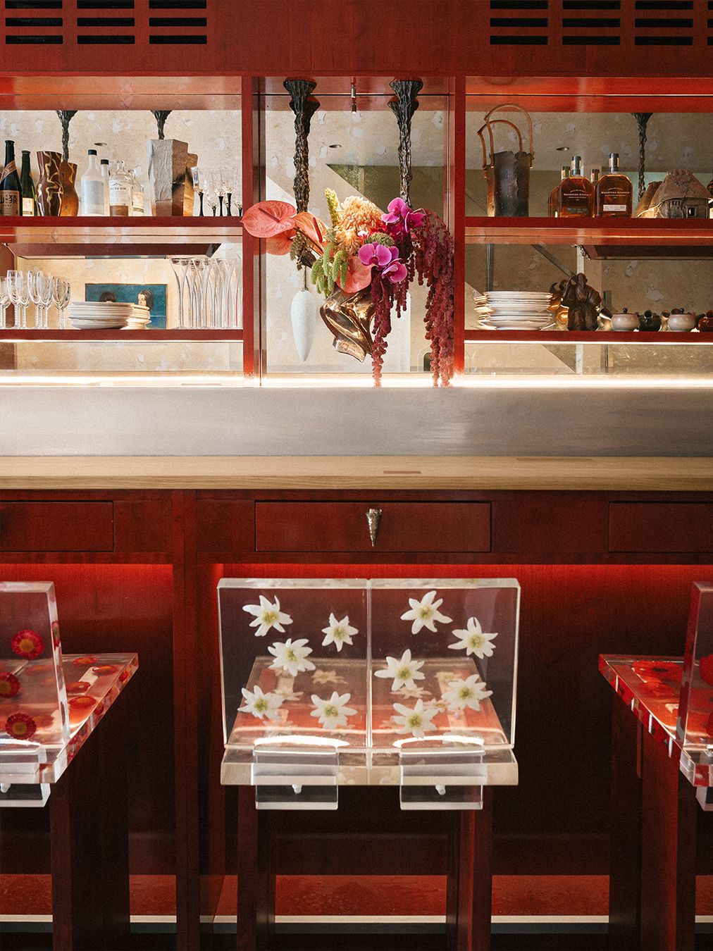 A red-painted wood and chrome bar of a restaurant, decorated with tall, geometrically cut wooden stools with flower-decorated resin backs.