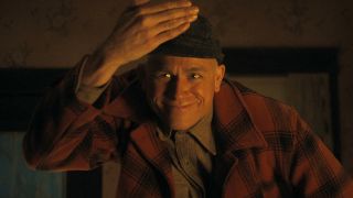 Ed Gein lifting hand from in front of his face and smiling in Monster: The Ed Gein Story