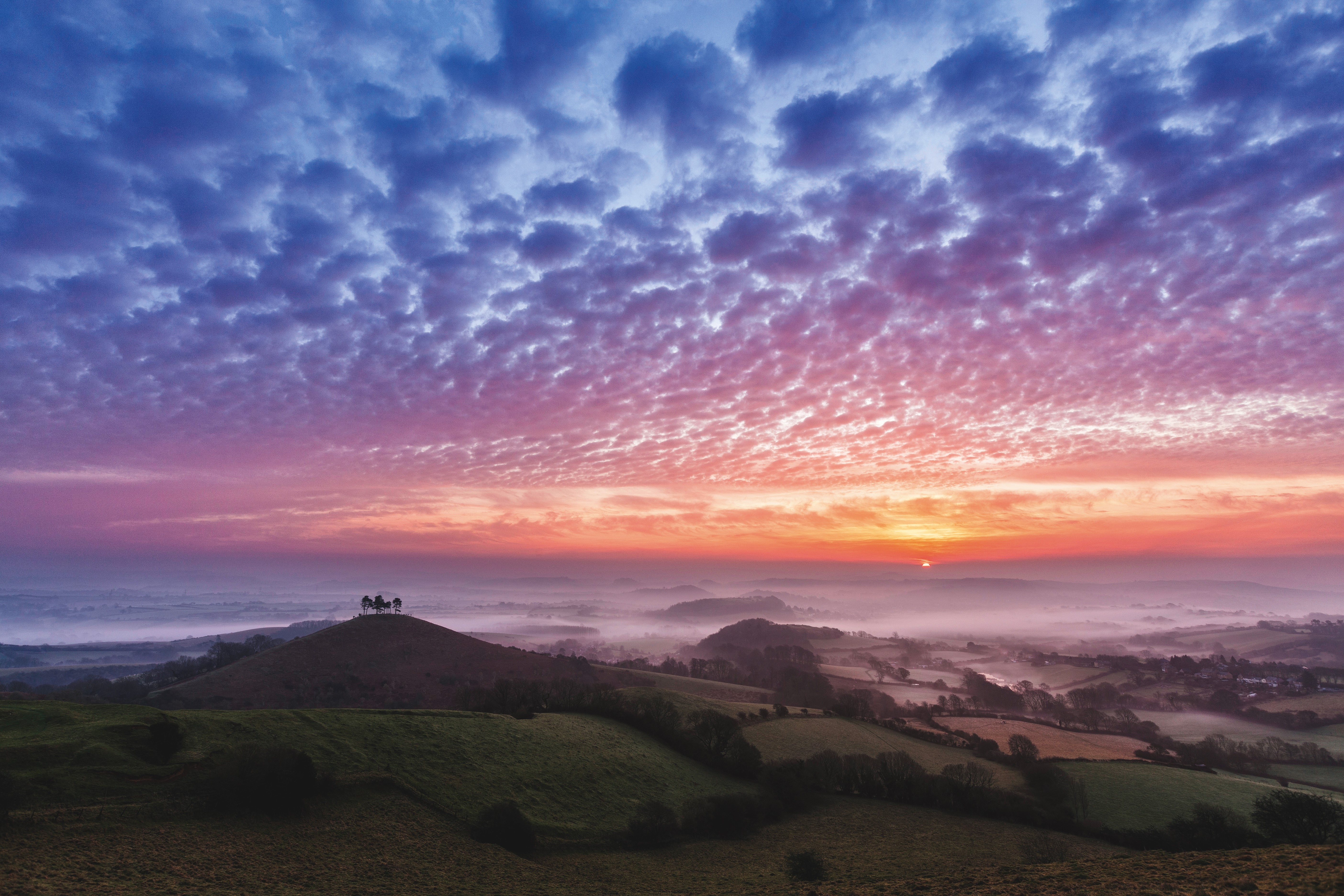 Sunrise over Colmer's Hill in dorset. A red and pink sky breaks over some green fields and hills
