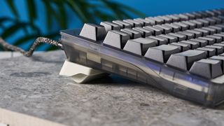 The Wooting 80HE in Ghost PCR case with black keycaps, on a stone surface with a blue background.