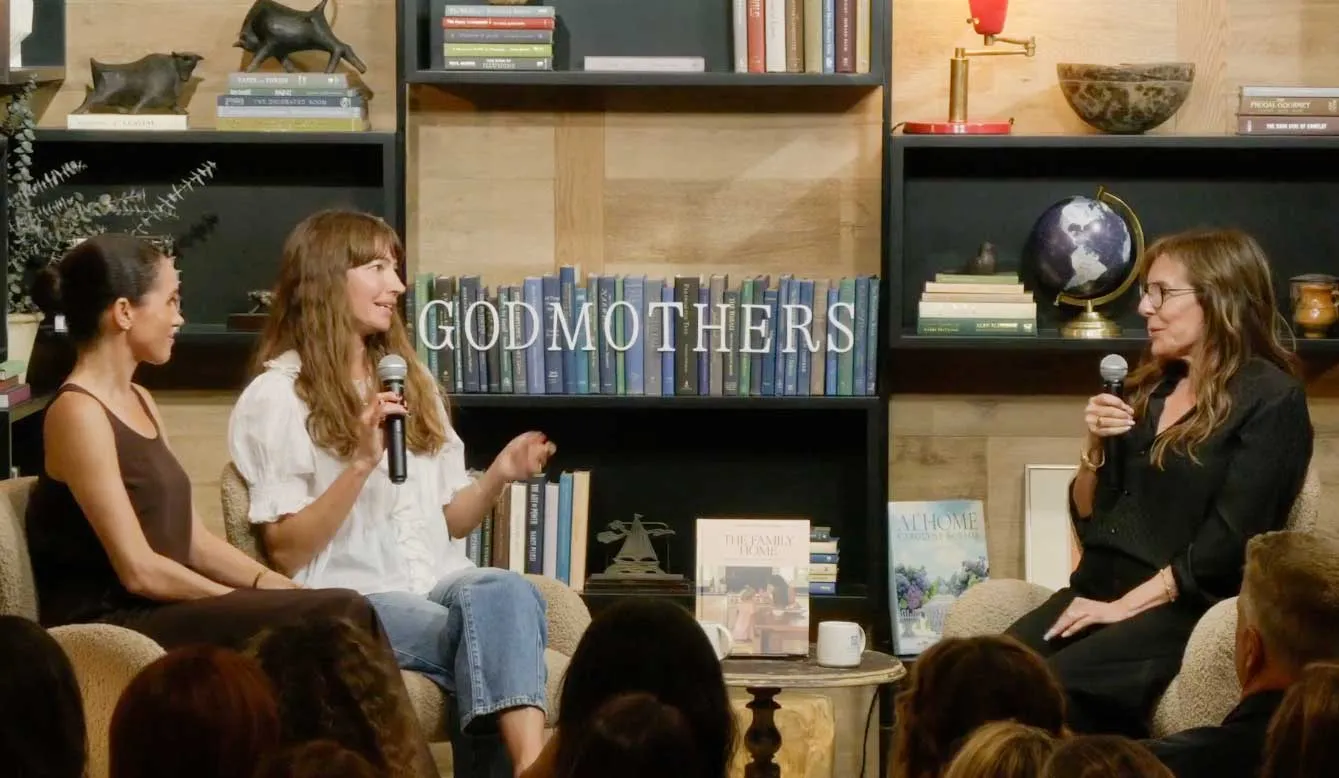 Meghan Markle sitting in a chair in a brown outfit next to author Courtney Adamo