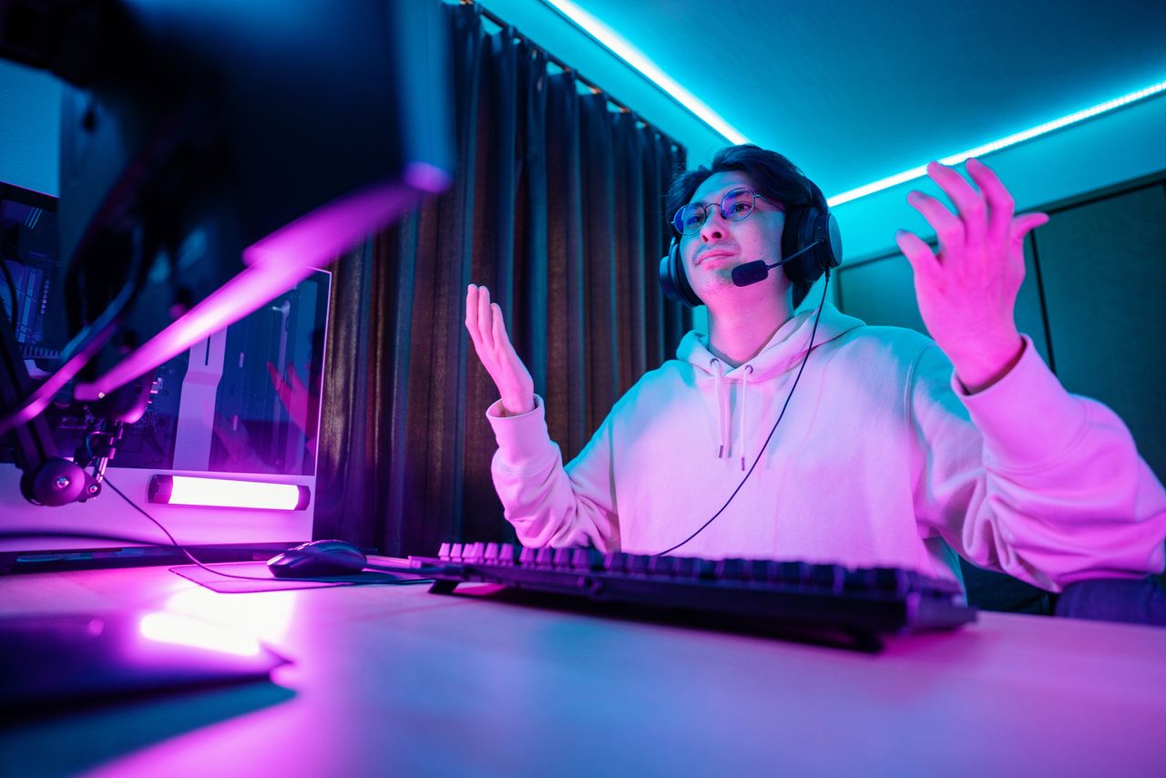 A man raising his hands in contempt while playing video games at his desk.