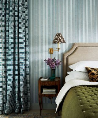 blue striped wallpaper in a bedroom with a linen headboard and forest green quilt