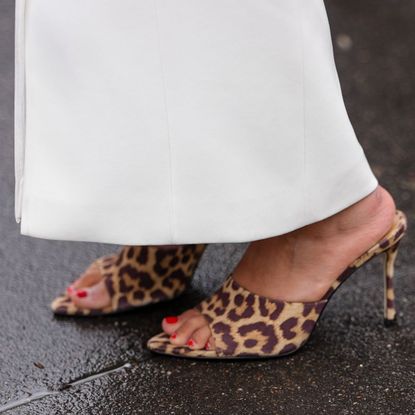 A close up of a woman's feet in leopard print heeled mules with painted red nails