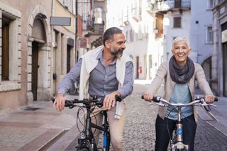 A mature couple bikes down a street in Italy.