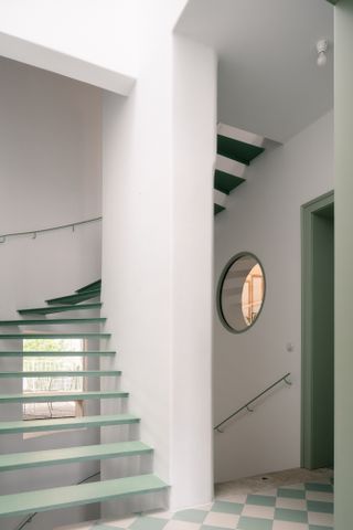 White landing with green floating staircase and porthole window