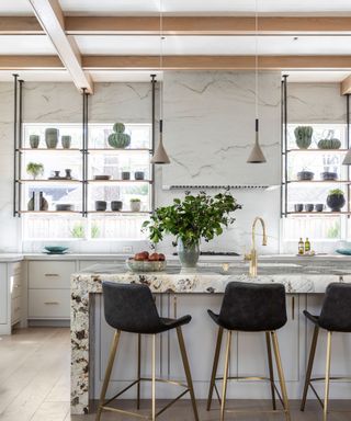 Large modern kitchen, island with marble countertop, bar stool seating, two large windows with open shelves, dressed with ornaments and accessories