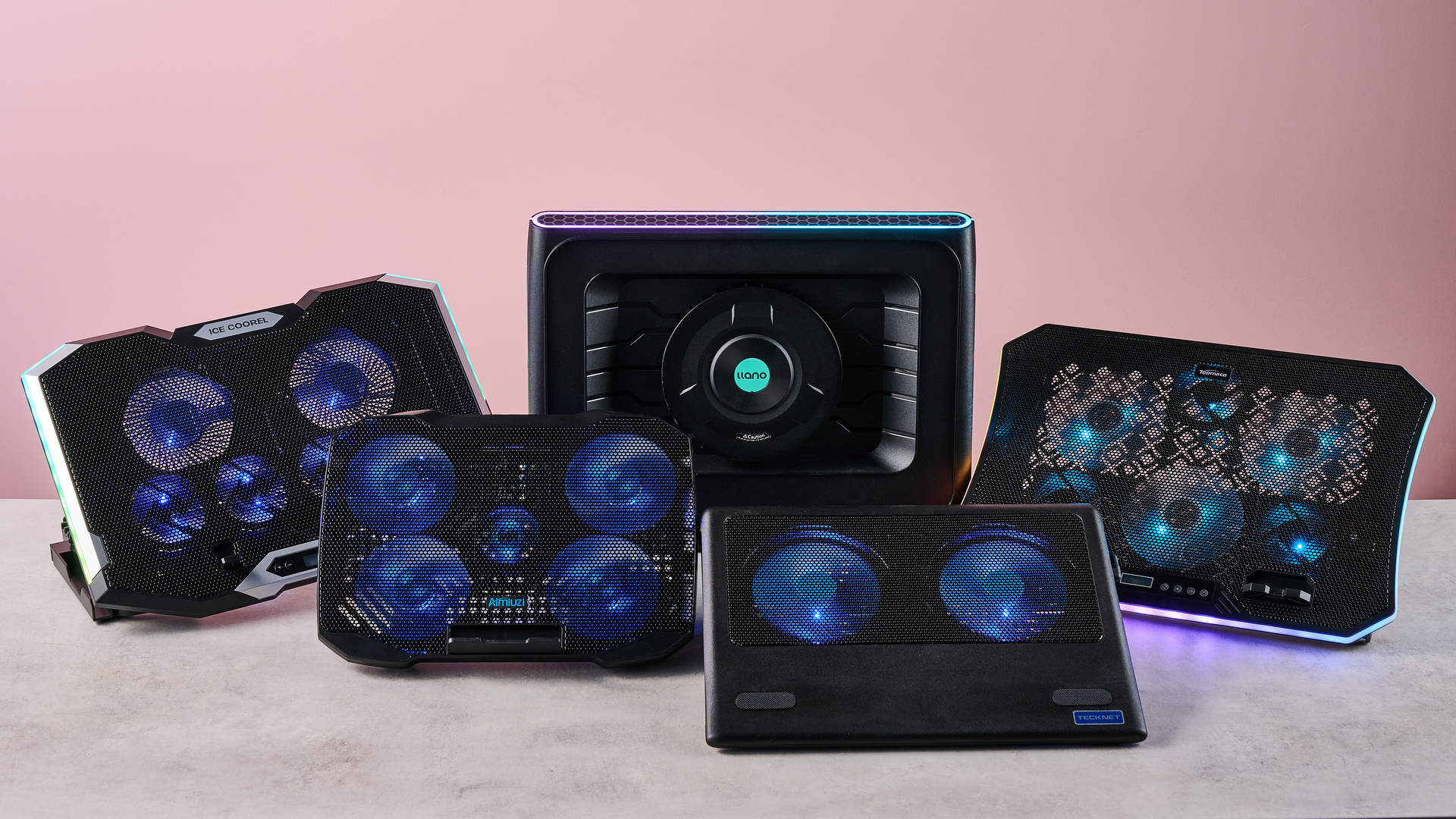 The Llano RGB Laptop Cooling Pad, TopMate C12, Aimuzi F2 Plus, ICE COOREL RGB Laptop Cooling Pad and Tecknet N8 on a gray marbled desktop in front of a pink background.