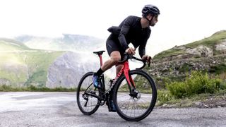 A male cyclist rounds a corner on a mountain climb while riding a red Pinarello F