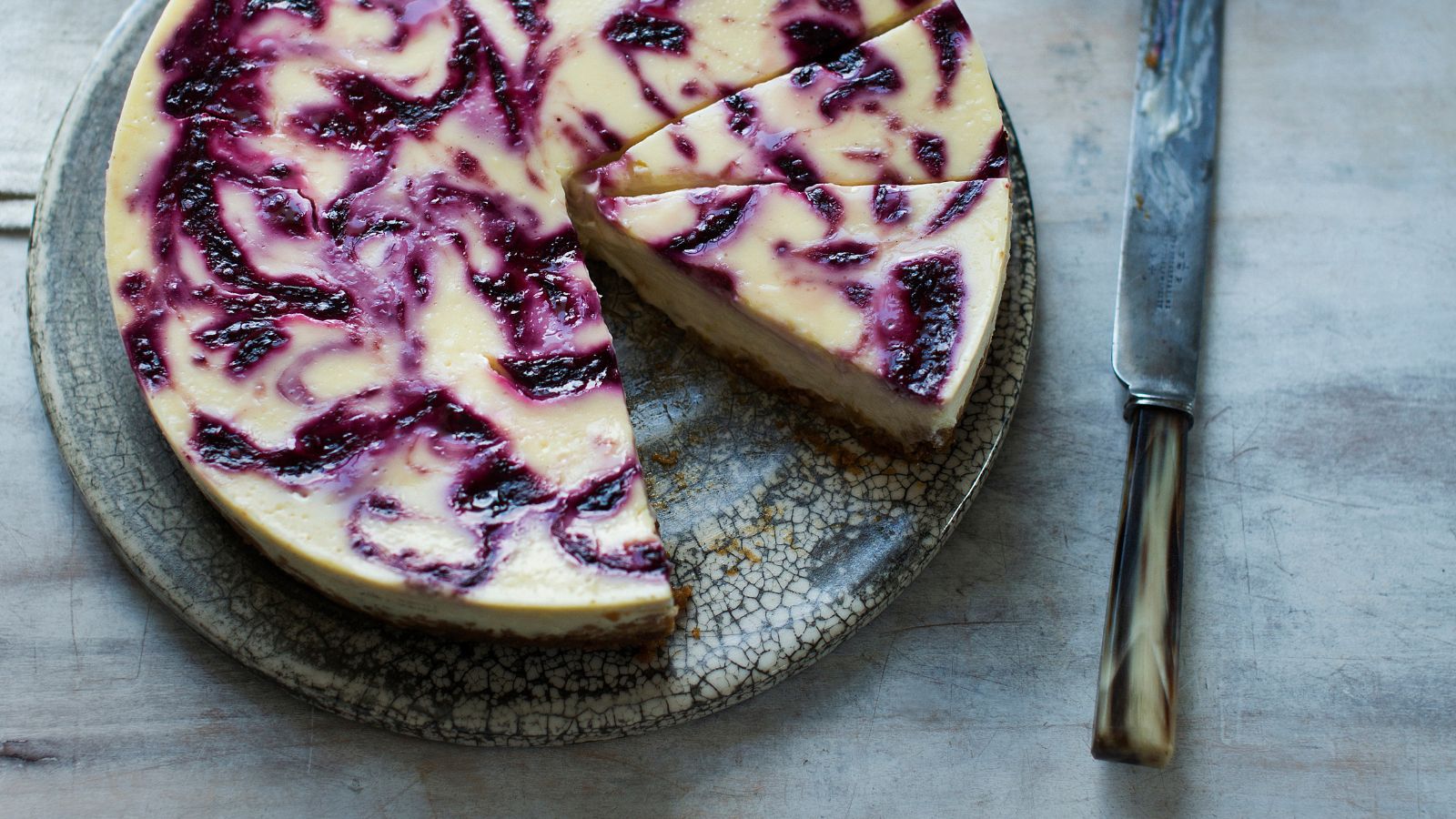 Blackberry cheesecake on a grey mottled plate next to a knife