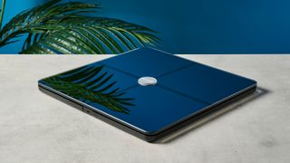 a modern black smart scale with a silver circle in its centre rests upon a light surface with a blue background