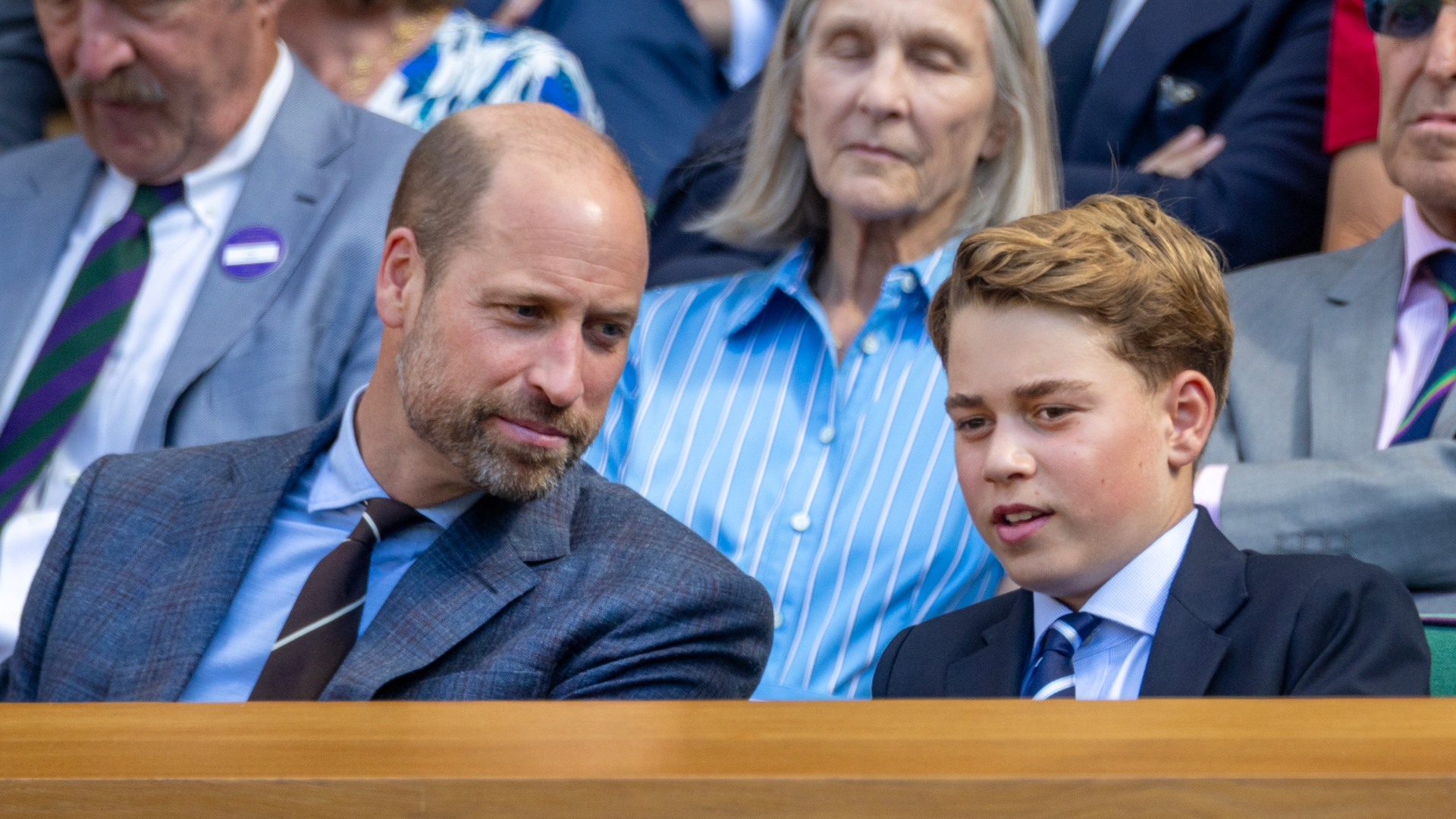 Prince William has a bald head and wears a suit while smiling at son Prince George as the pair attend Wimbledon 2026