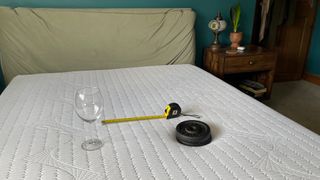 Testing motion isolation using a weight, empty wine glass and a tape measure for our REM-Fit Pocket 1000 Mattress review