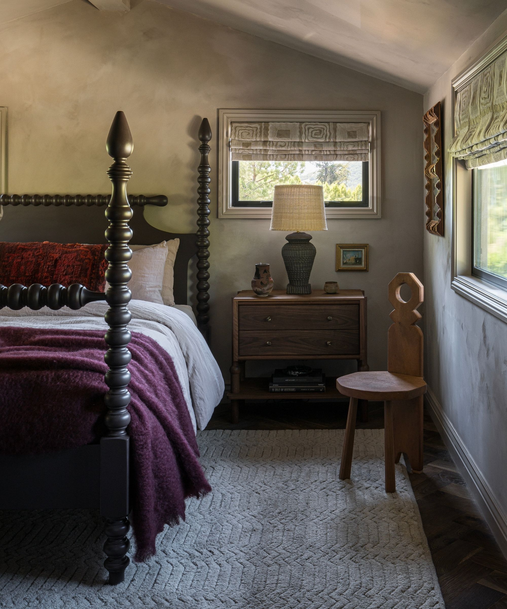 a moody gray limewashed cottage bedroom with dark antique wooden bed and purple blanket