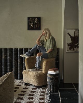 Interior designer Montana Labelle sitting on the armrest of an armchair chair in her living room