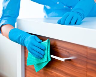 Close up of woman's arms cleaning and polishing kitchen cabinets with blue gloves and a green cloth