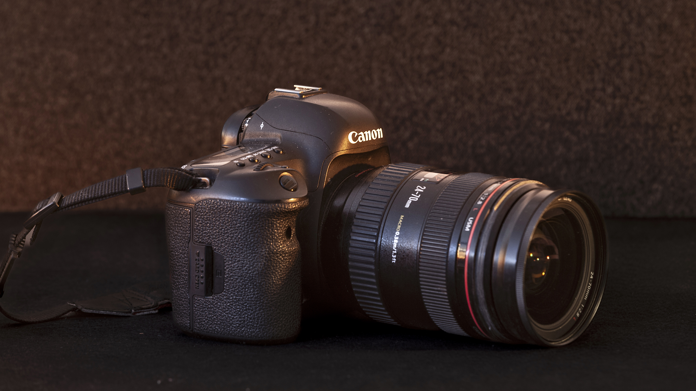 A DSLR camera with a zoom lens lies on a dark surface. The camera is angled to the right