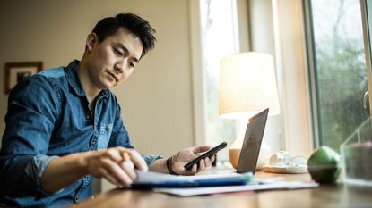 A man looks at a computer with a calculator. 