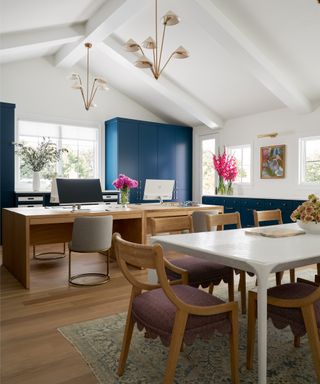 Home office with vaulted ceiling with two chandeliers, large desk and table and chairs