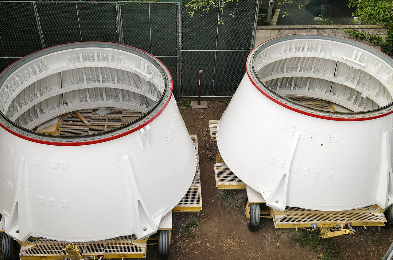 two large white cylindrical objects, known as aft skirts, sit atop small wheeled carts