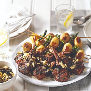 BBQ meat and potatoes and asparagus on skewers on white plate on white wooden table