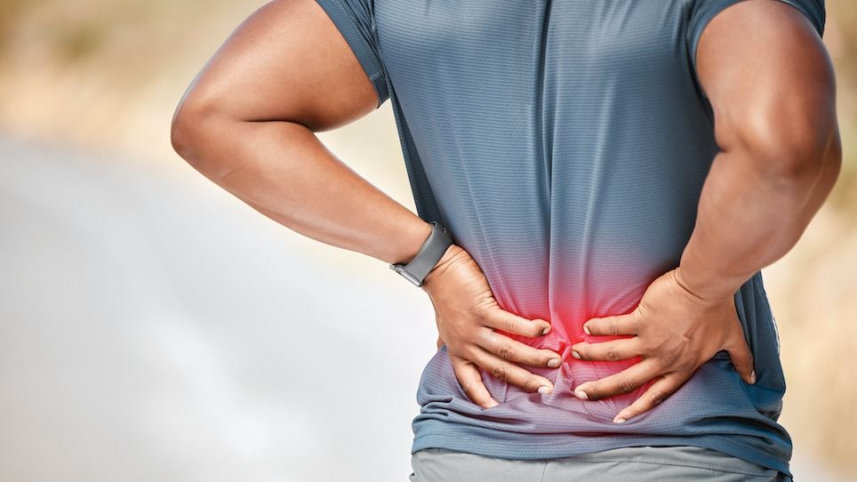 A man holds his back in pain; red highlights the site of his pain in his lower back