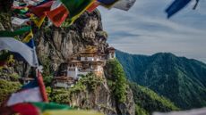 Prayer flags wave in the wind with Bhutan's Tiger's Nest monastery in the distance