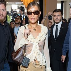 Bella hadid wears a white ruffle blouse and a brown coach bag.