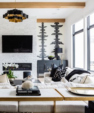 Black and white living room with black credenza in alcove, black cushions, tv, fireplace, bold wallpaper, white couches, black pendant light,