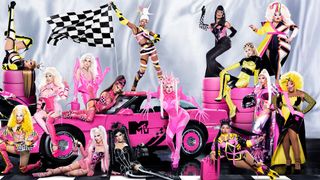 The cast of RuPaul’s Drag Race season 15 posing in front of a pink car, a checkered flag and pink tires