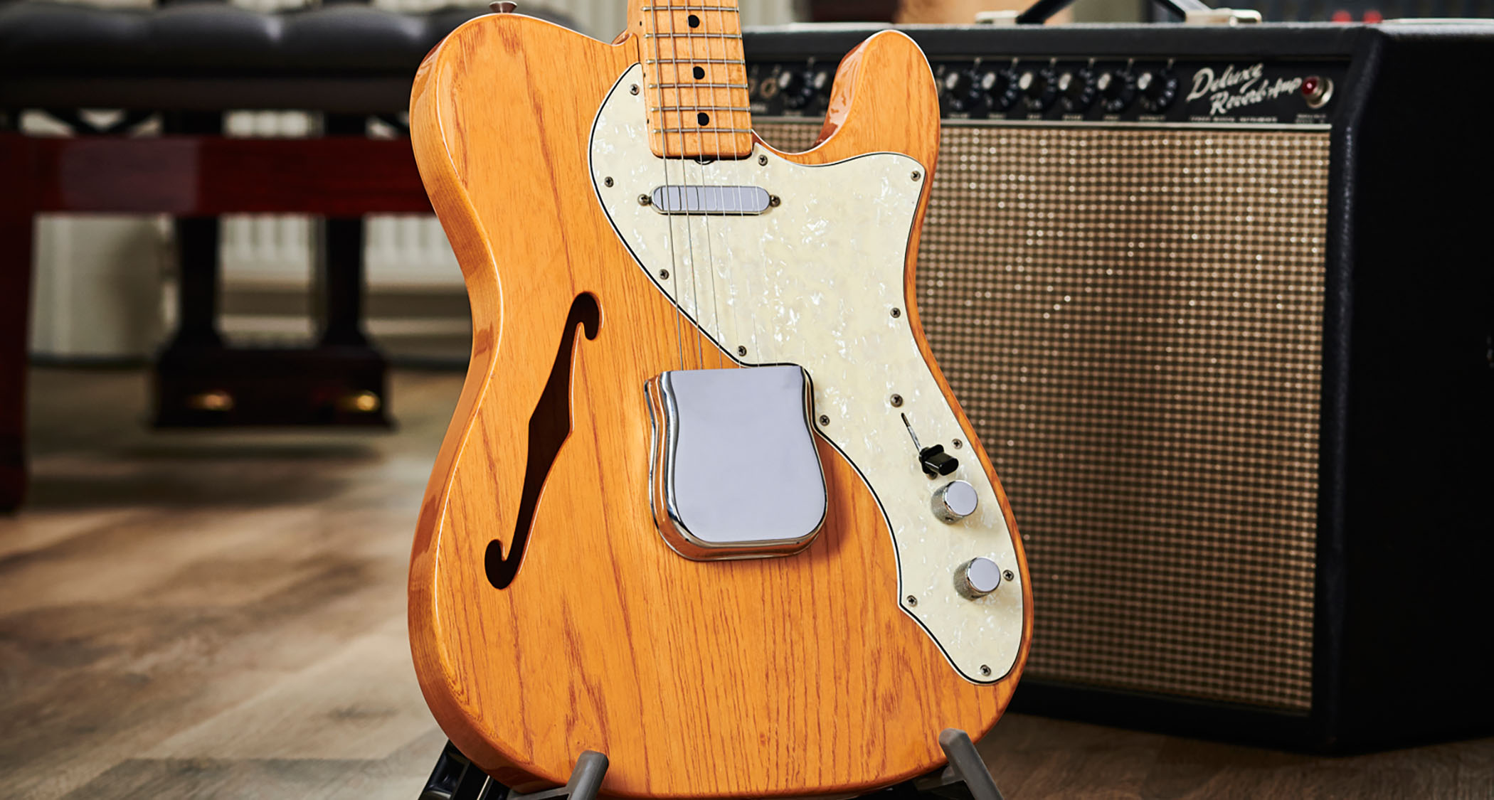 A vintage Fender Telecaster Thinline in natural finish sits in its guitar stand, in front of a Deluxe Reverb tube combo