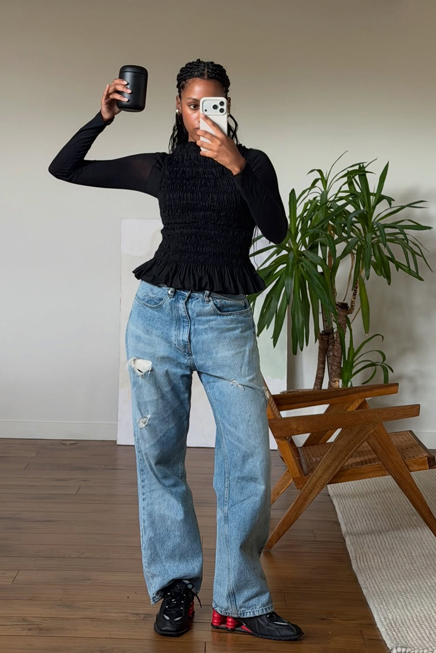 a woman wearing a shirred black shirt, blue baggy jeans, and black and red Nike sneakers