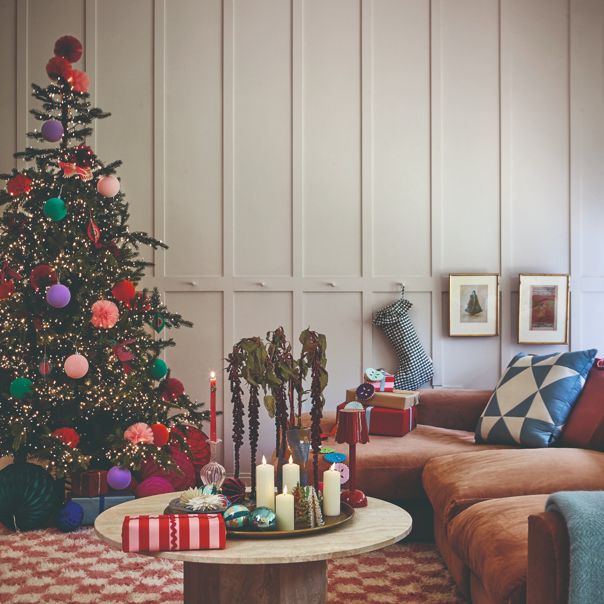 A living room with a brown chaise sofa decorated for Christmas with a lit-up Christmas tree, presents and a Christmas stocking 