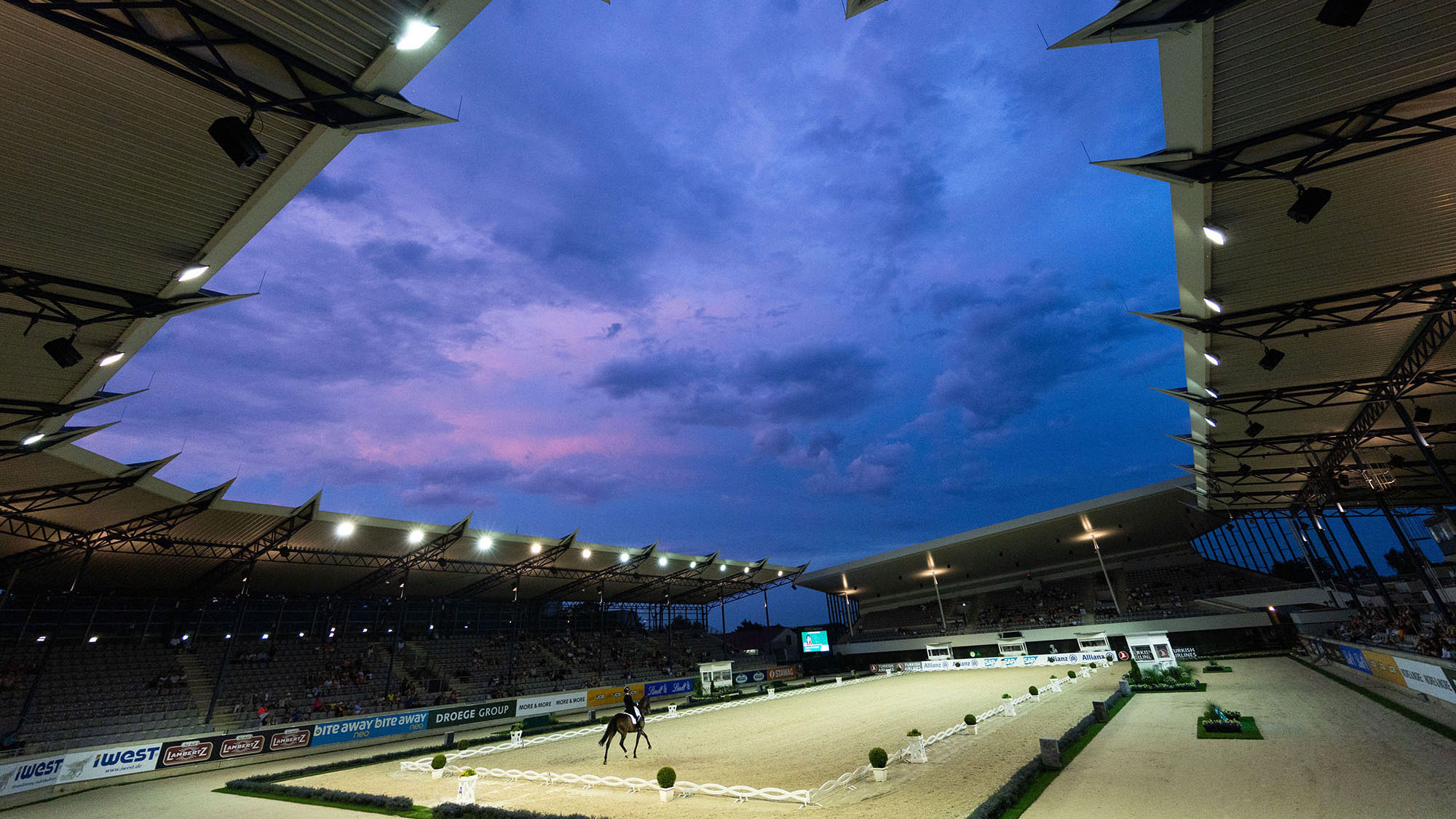 The view from the stands in the Aachen dressage arena as a horse performs under floodnight with the night sky above.