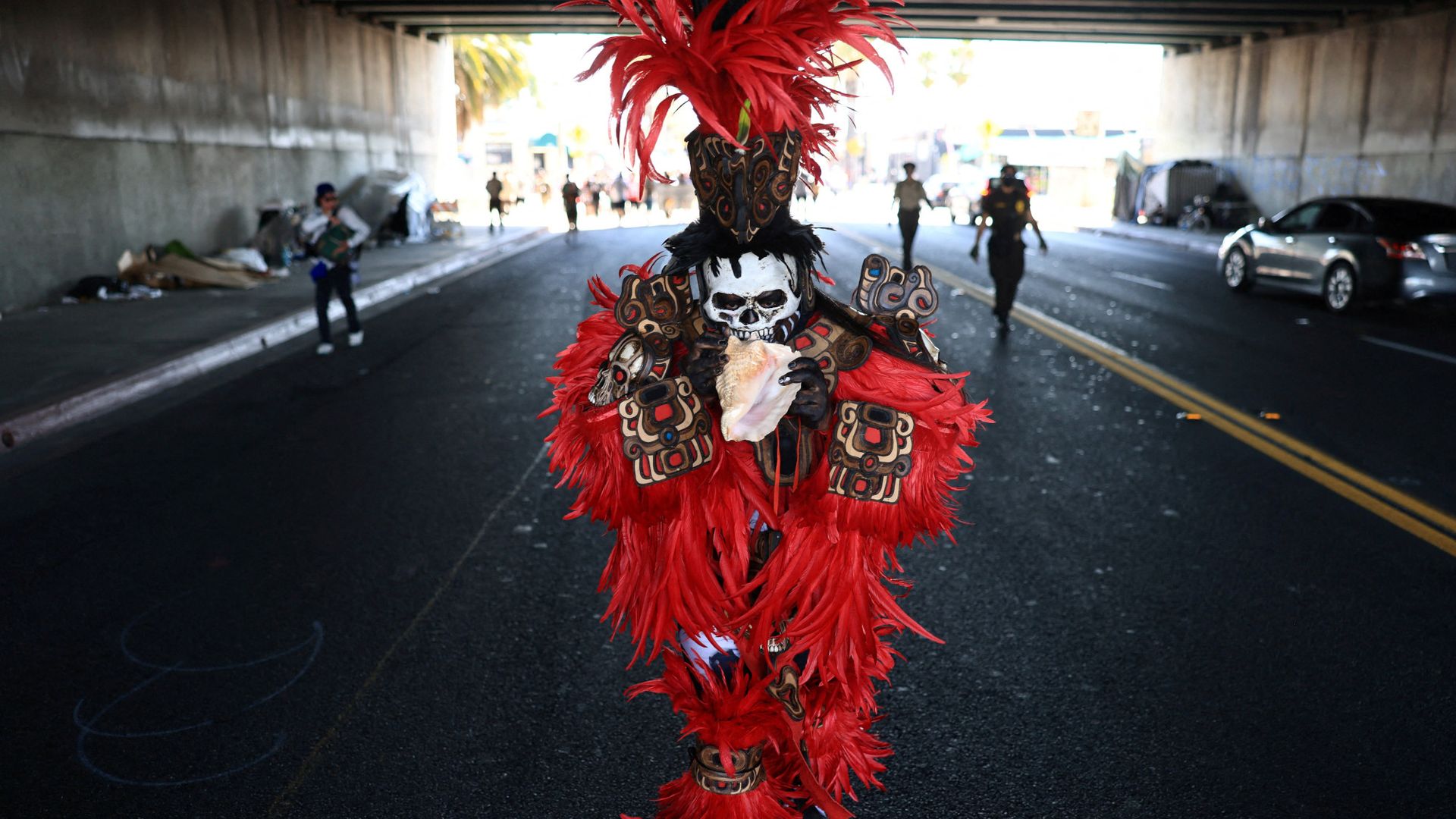 
                                A costumed figure blows into a conch shell during the 55th National Chicano Moratorium in Los Angeles
                            