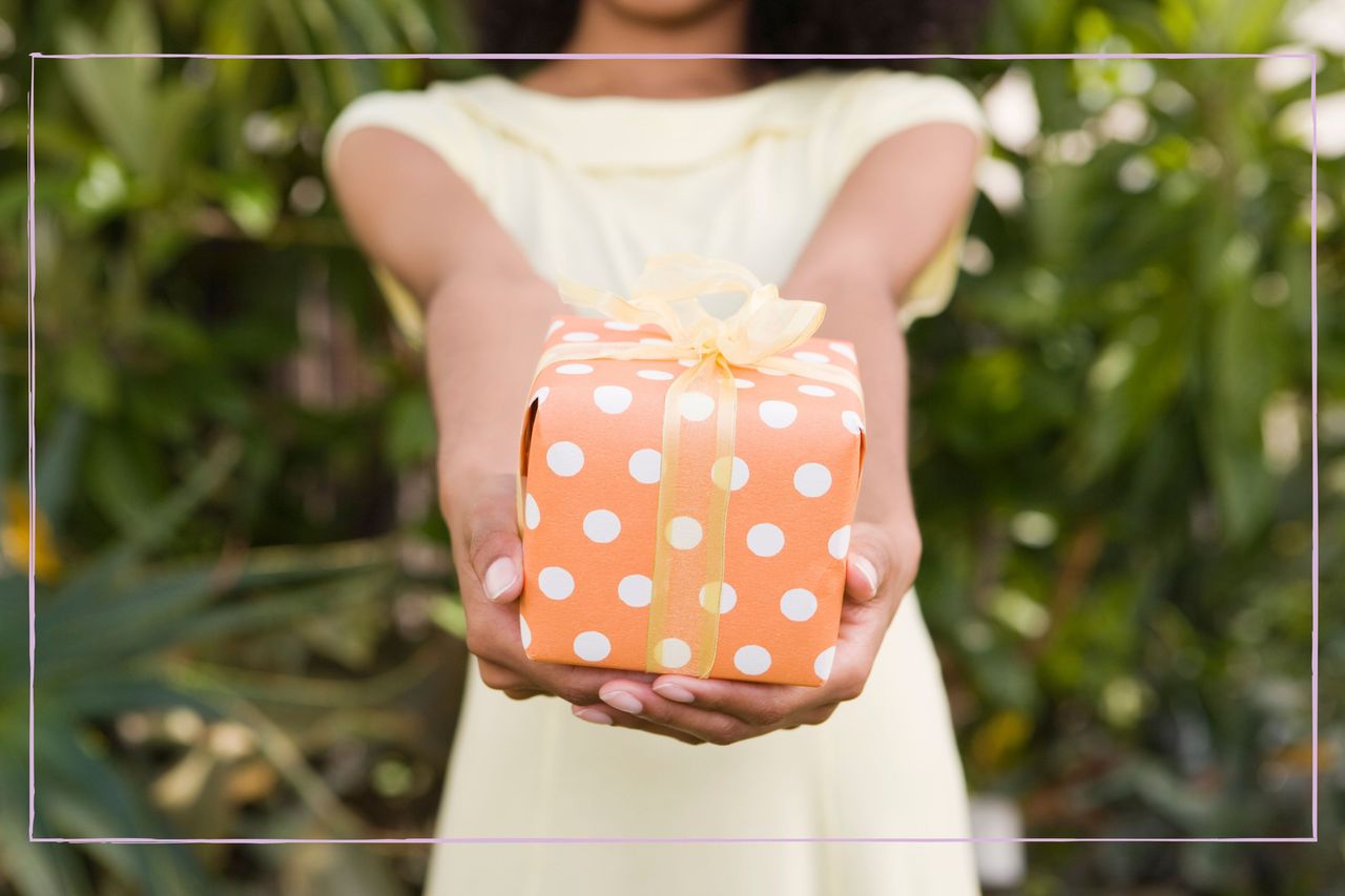 a close up of a female&#039;s hands holding a wrapped present with an orange bow and spotted wrapping paper